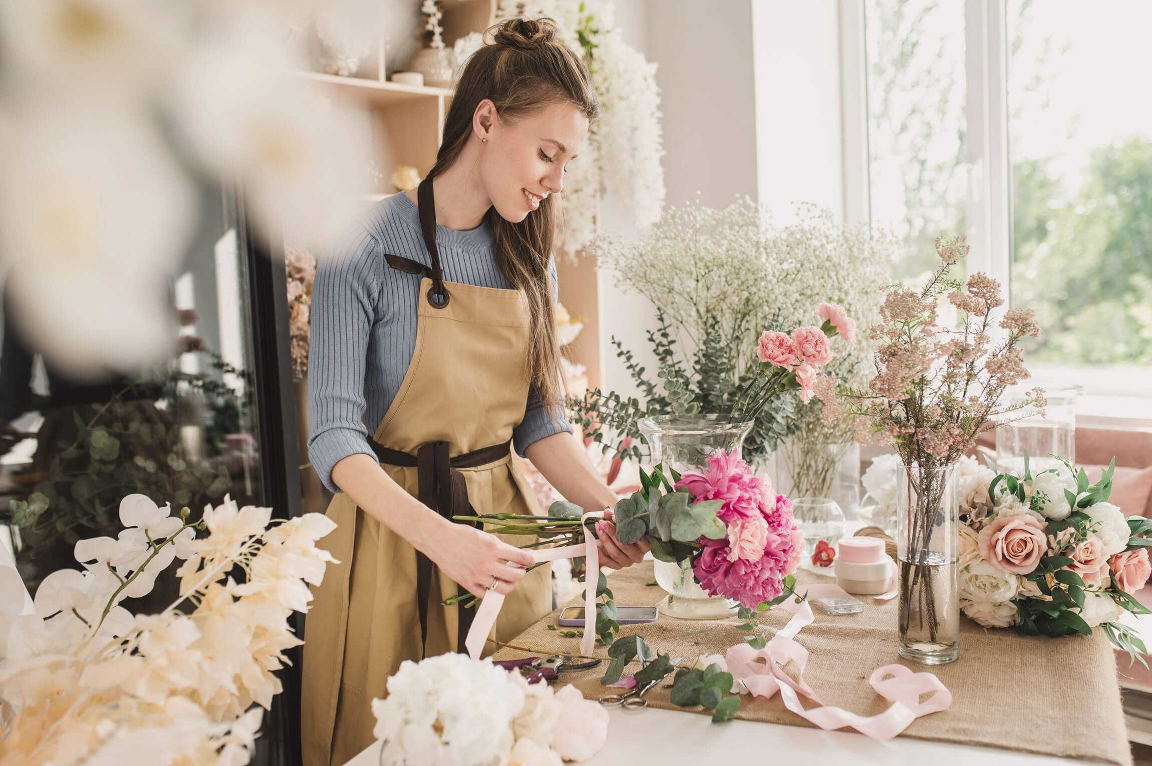 A florist in an apron arranging a bouquet at a workbench in a flower shop, absorbed in the task.